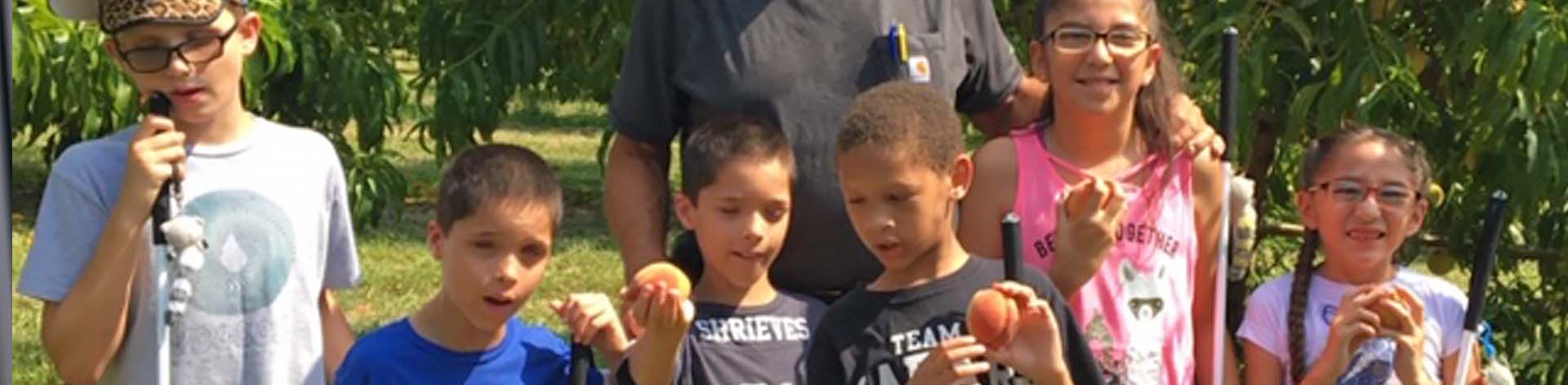Six blind children of varying ages smile while holding fresh peaches during a farm outing