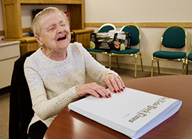 A senior blind woman smiles as she reads a Braille book